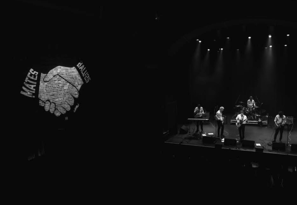 The MATES handshake projected on the brick wall while the band plays at the 2025 Mates Ball, The Princess Theatre
