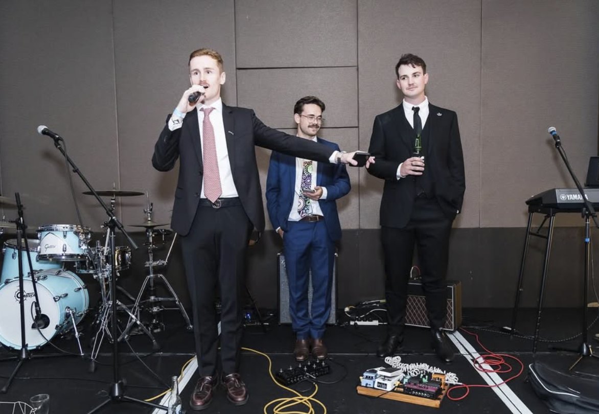 Harry Hooper on the mic with the band behind him at the Harry Hooper Ball, 2023