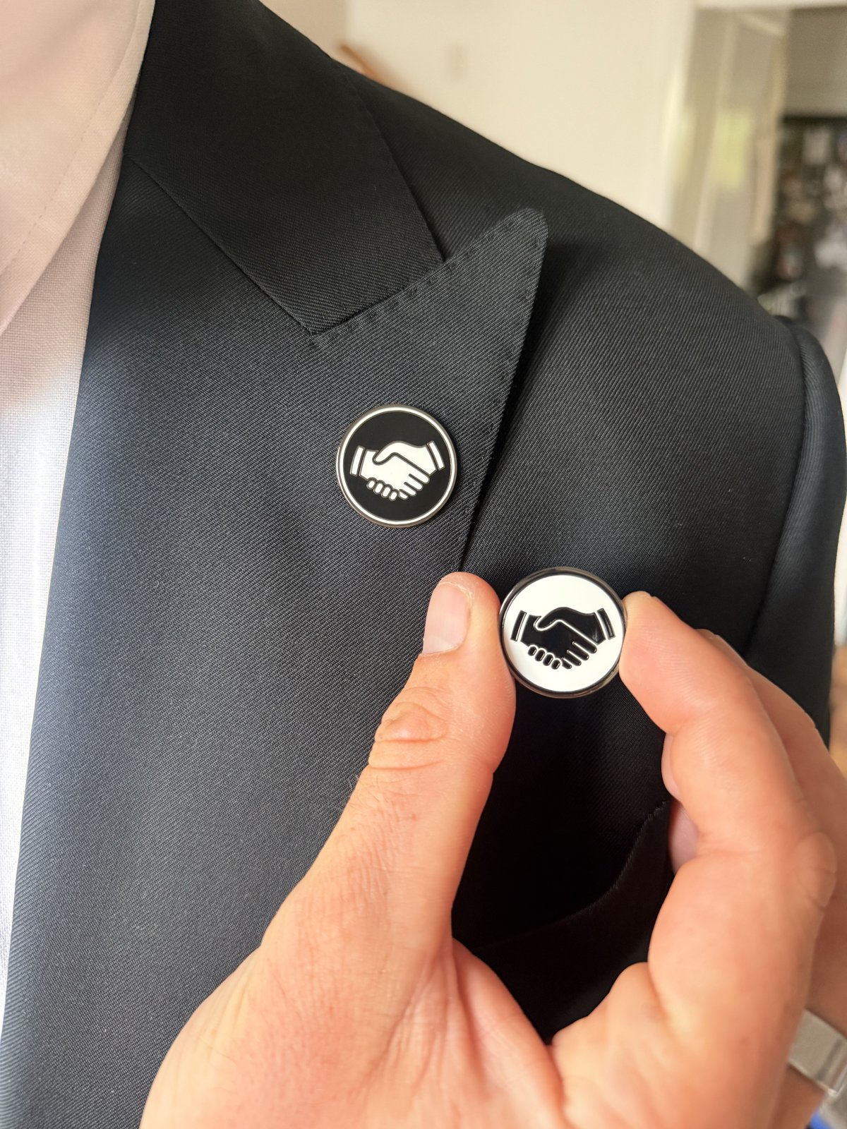 A black Mates pin held in a hand