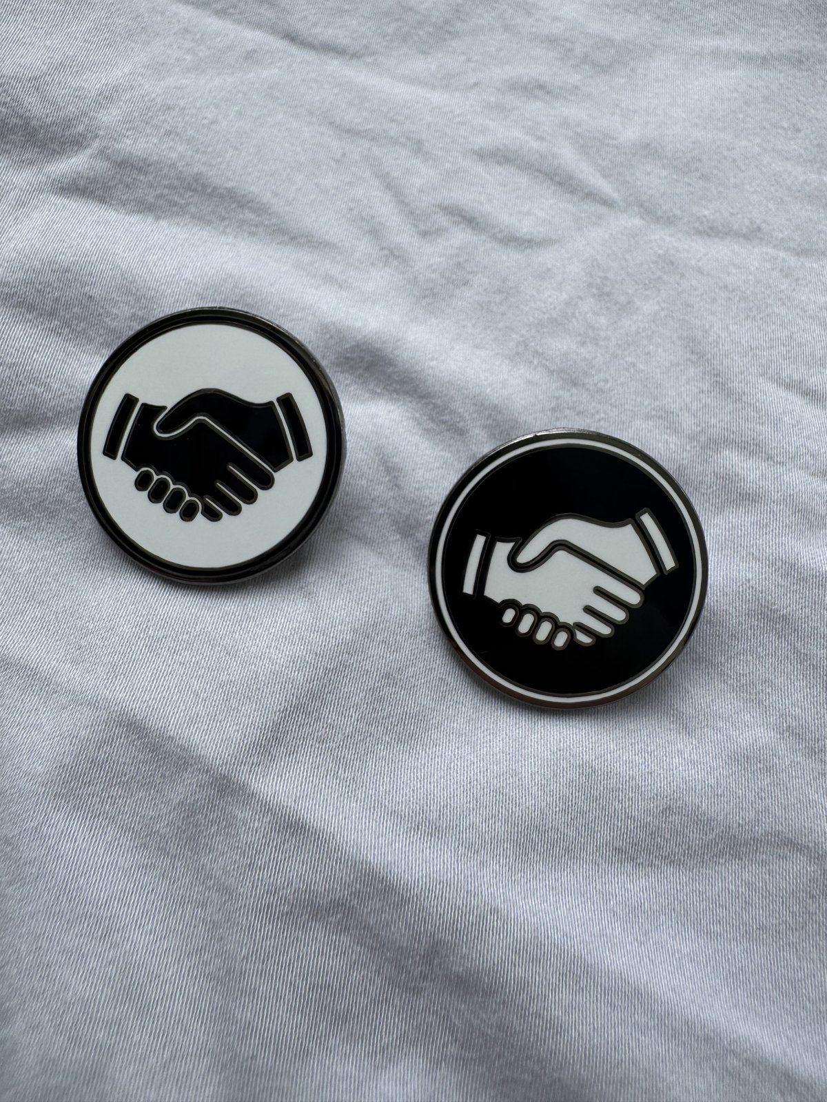 A white and a black Mates pin side by side on white linen